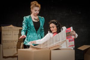 woman standing over girl reading newspaper